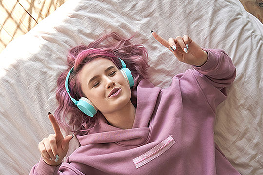 Foto: Ein Mädchen liegt mit Kopfhörern auf dem Bett und hört Musik.