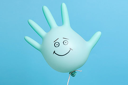Ein fünffingeriger Gummihandschuh ist wie ein Luftballon aufgeblasen. Auf die Handfläche ist ein Smiley gemalt.