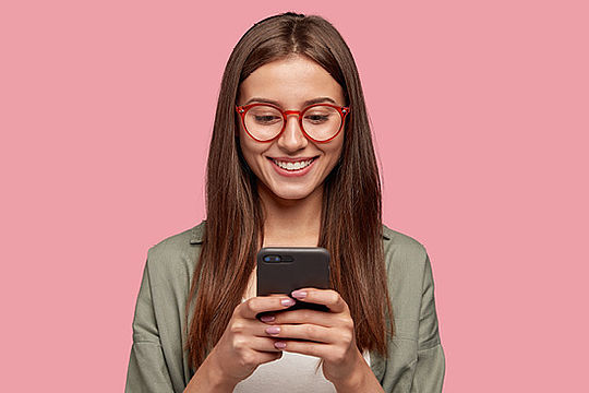 Ein Mädchen mit Brille schaut lachend auf ein Handy in ihren Händen.